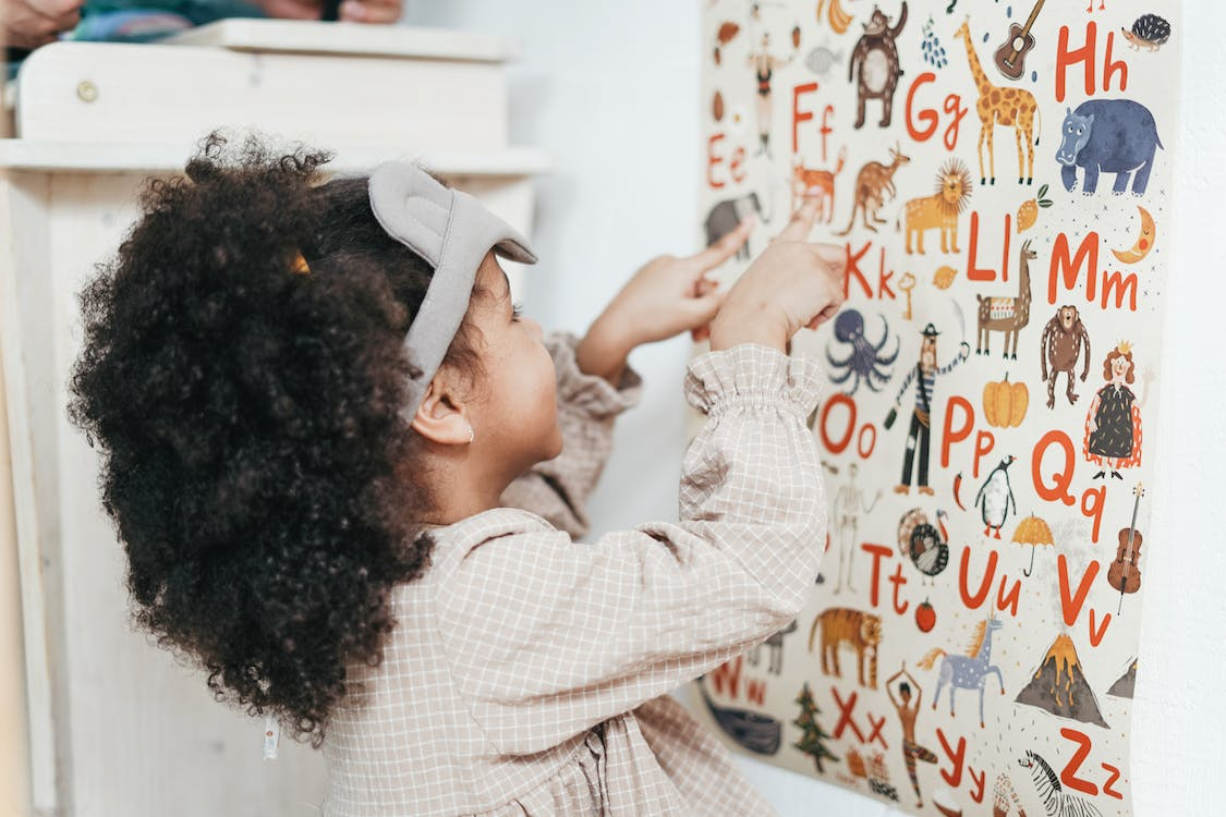 A little girl pointing at pictures on a wall.